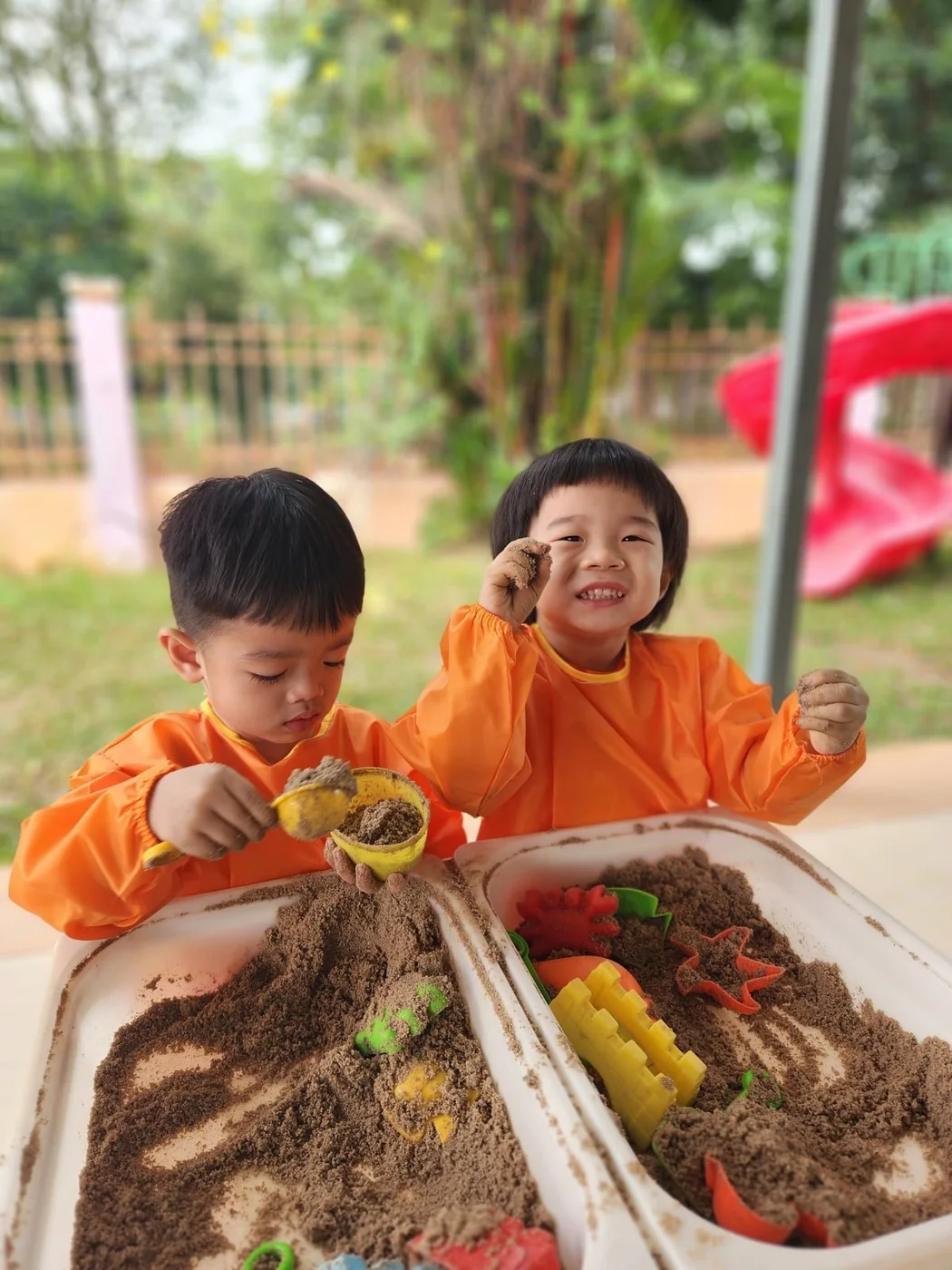 Young children exploring sand with scoops.