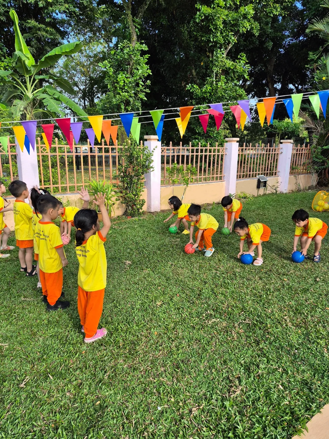 Children playing with colourful balls on a lawn under bunting.
